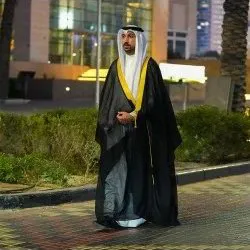 Man in a black bisht with gold collar at night