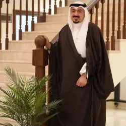 Man in a dark brown bisht beside a staircase