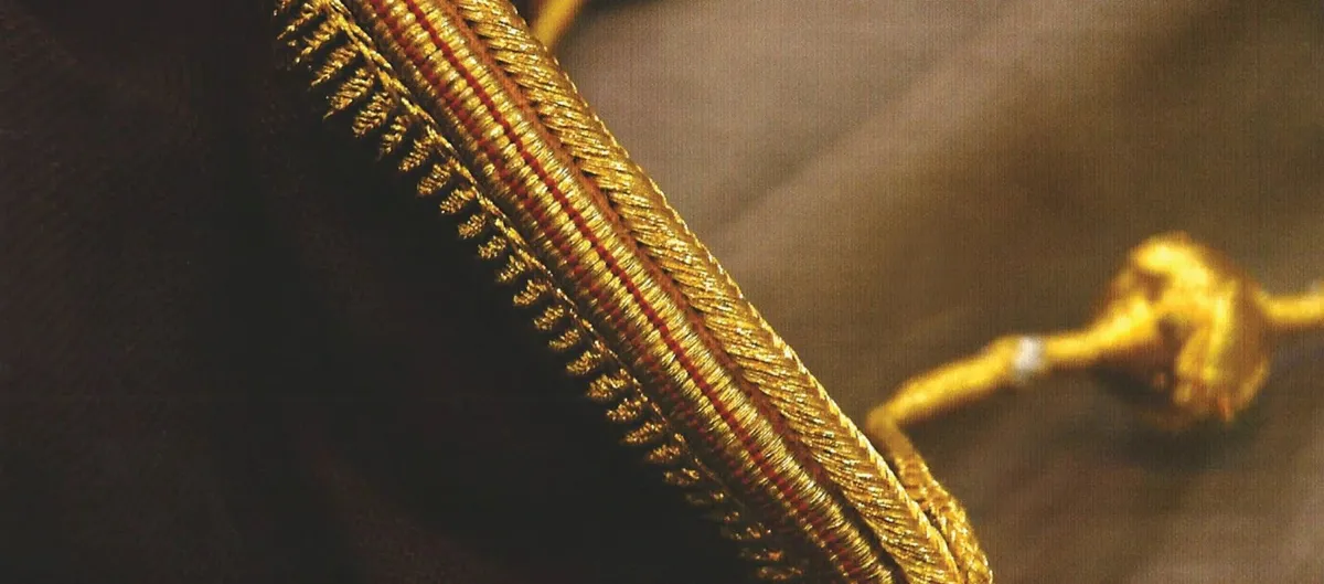 Close-up of gold zari edging on a dark brown bisht