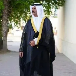 Man in a black bisht with gold collar on a tree-lined street