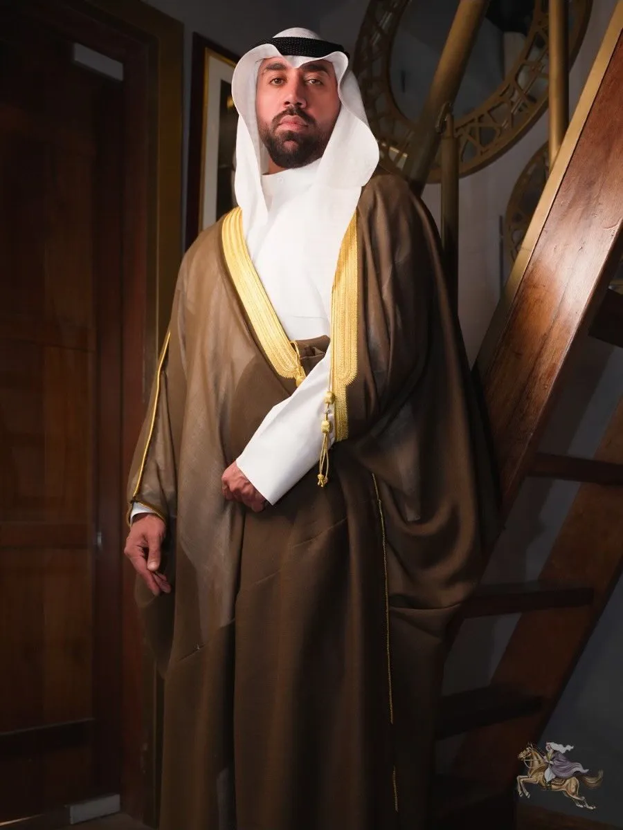 Man in a brown bisht with gold zari standing on a wooden staircase